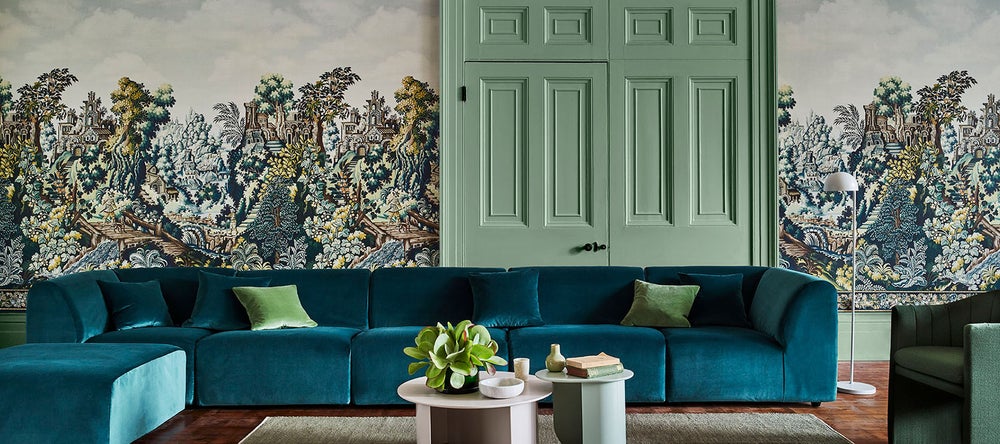 Rauminszenierung mit gemusterter Cole & Son Tapete, grünen Wandpaneelen und blauem Sofa